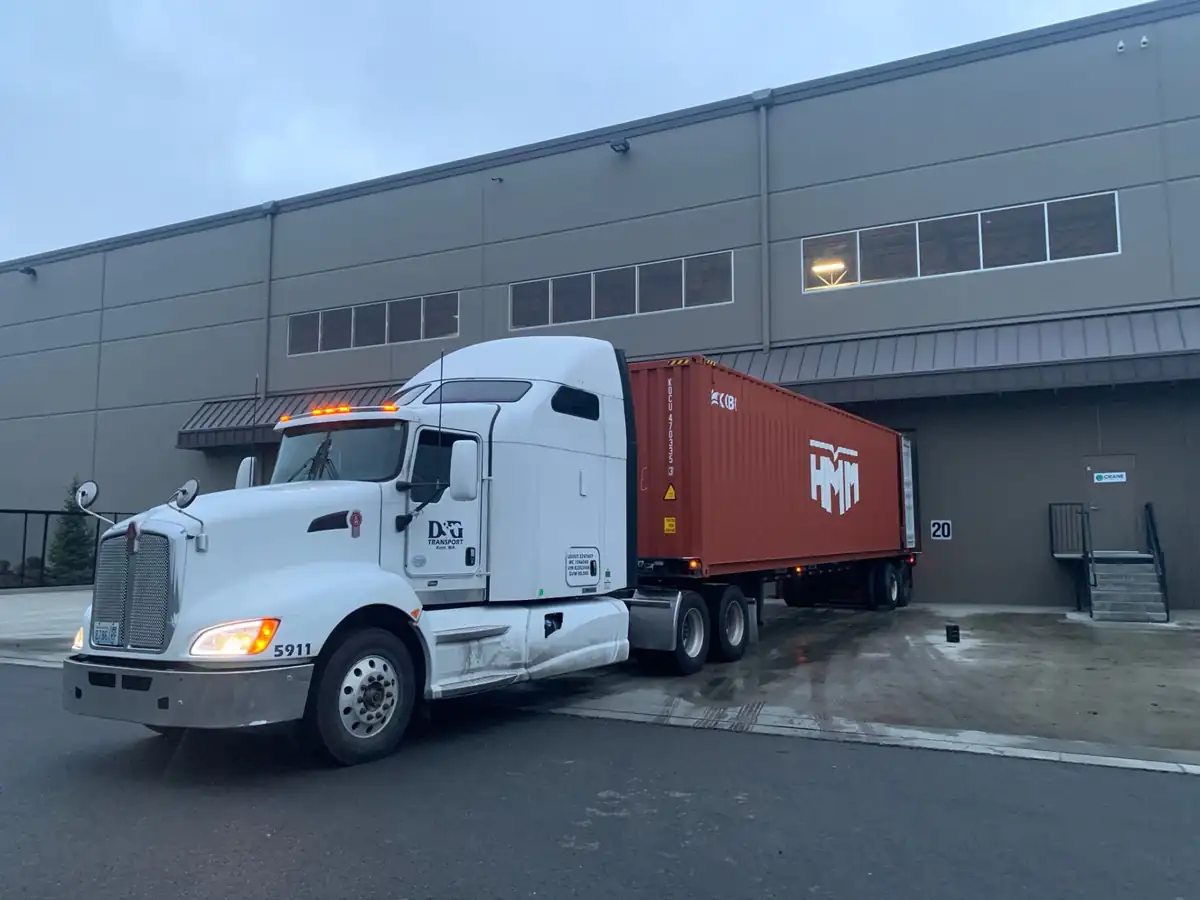 D&G Transport Kenworth backing an HMM ocean container into a warehouse dock door