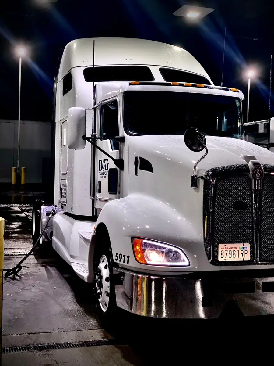 Freshly washed white D&G Transport Kenworth tractor under floodlights at night