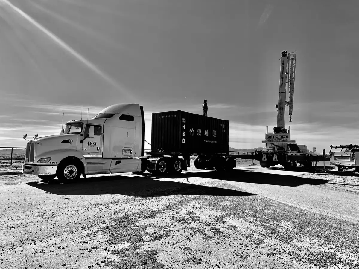 Crew member standing on an ocean container while a crane prepares to lift it off a D&G chassis