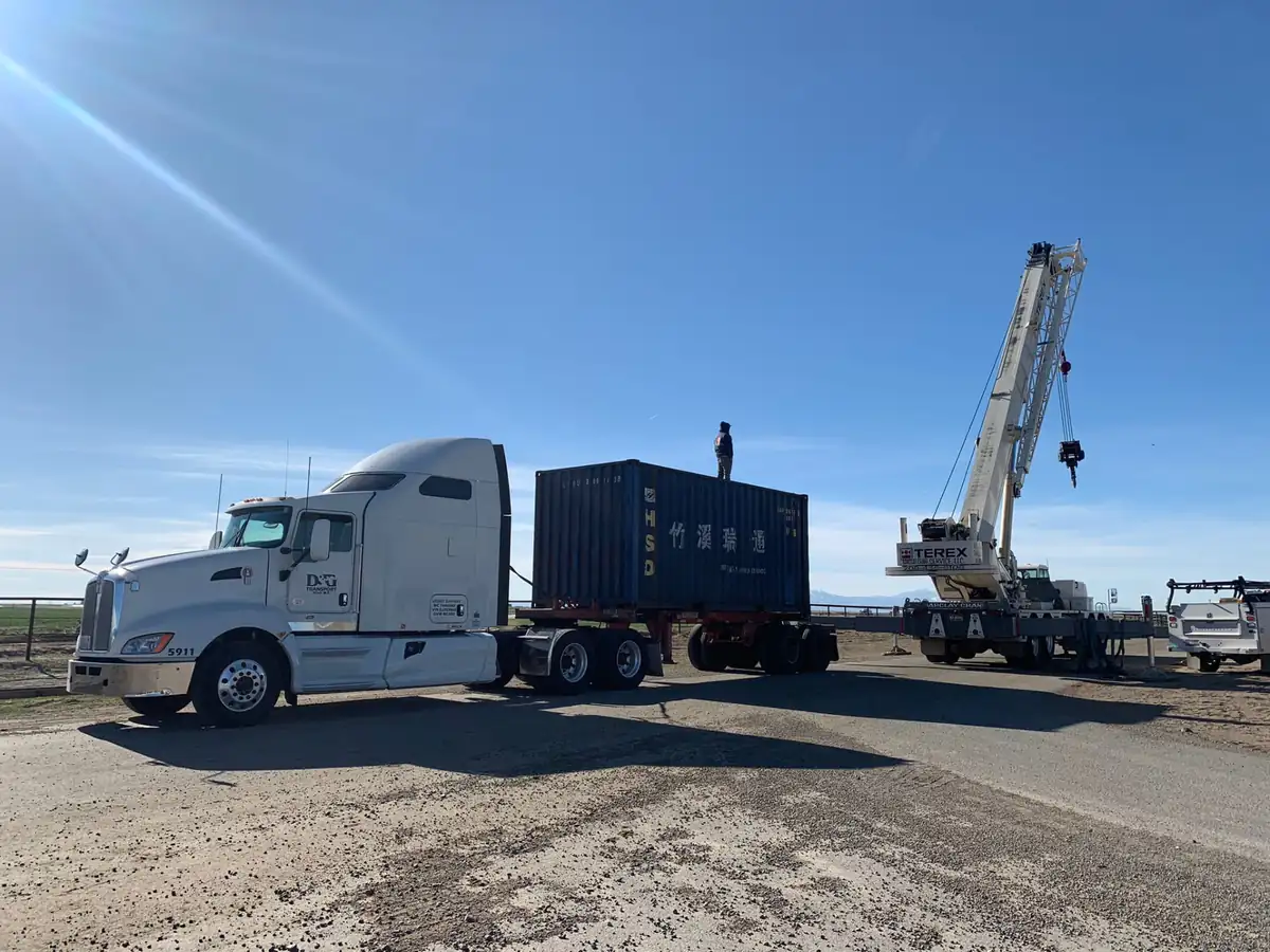 Terex crane setting an ocean container beside a D&G Transport tractor on a clear day