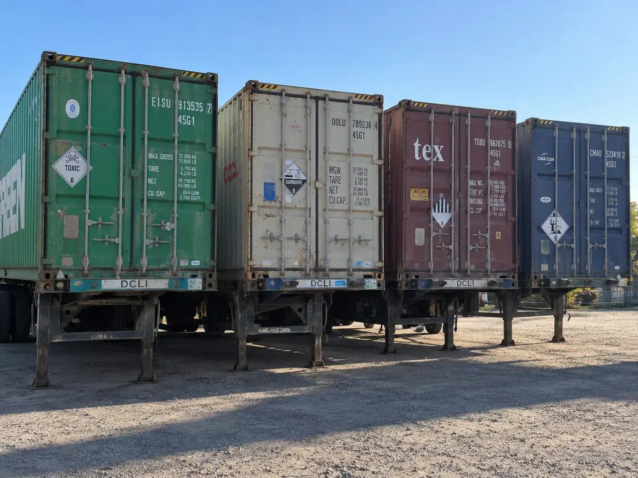 Four containers on chassis displaying hazardous materials placards, including toxic, corrosive and class 9